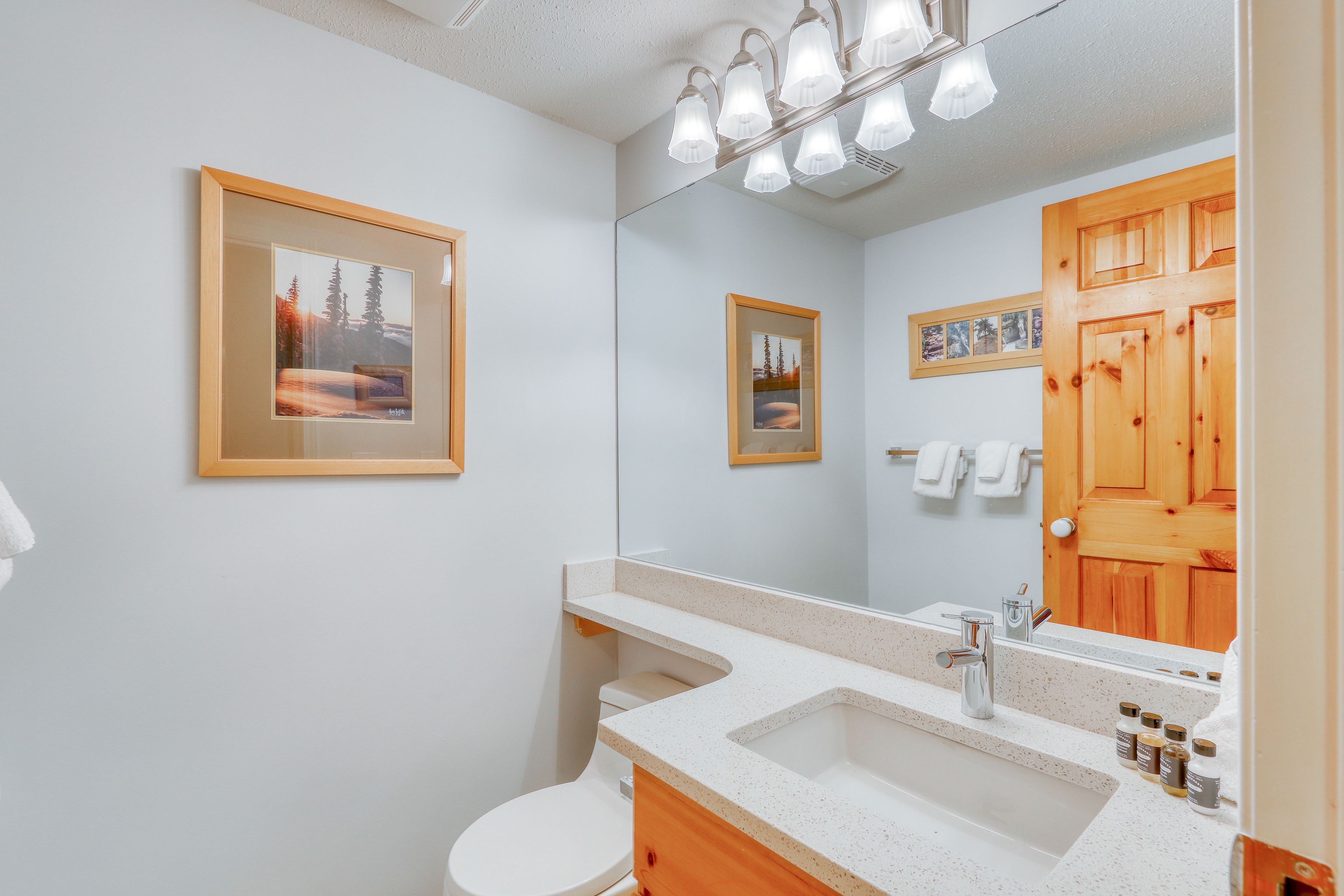 Un baño moderno con lavamanos blanco, tocador de madera y un espejo grande.
