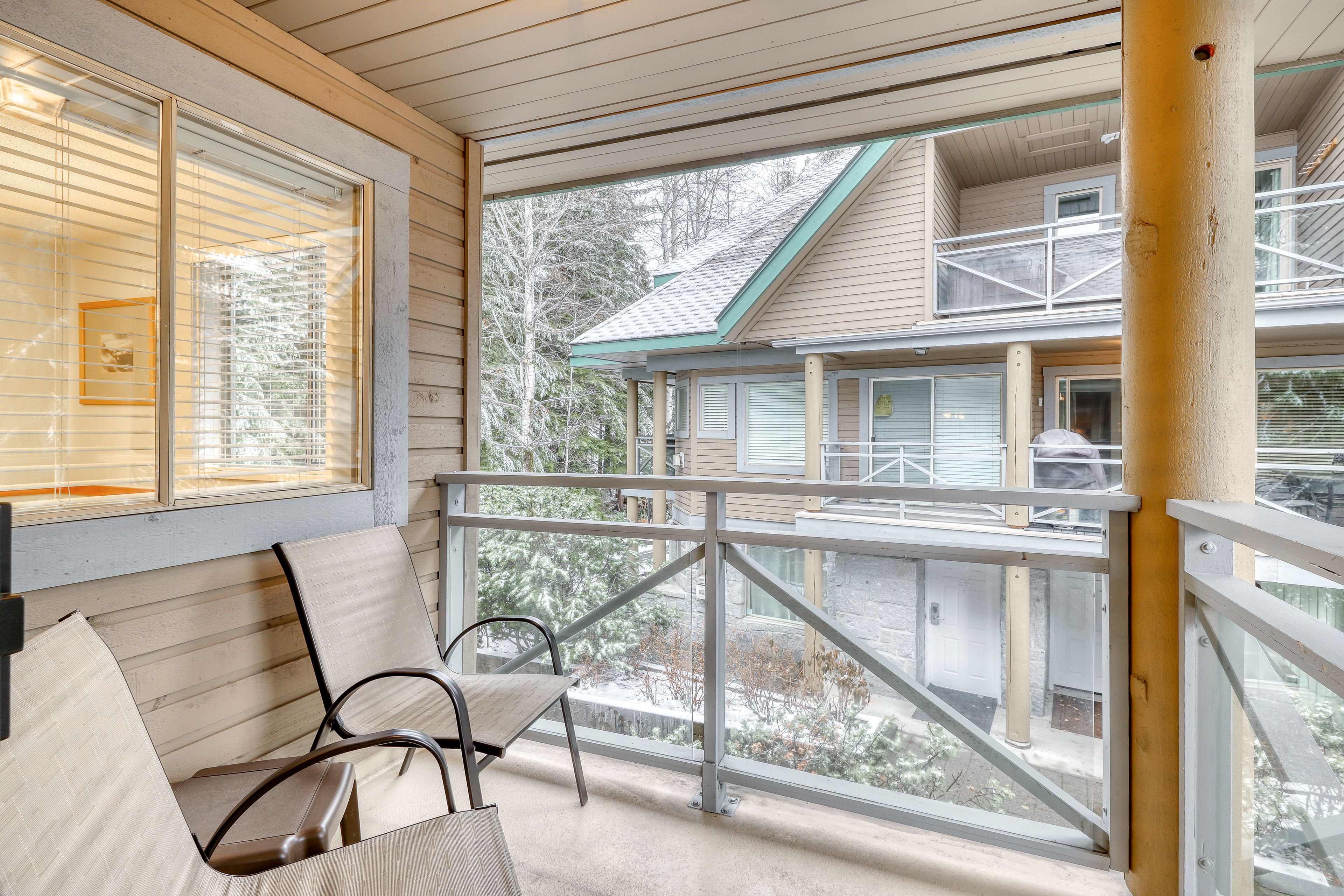 A covered porch with a view of a two-story building, a chair, and a wooden bench.