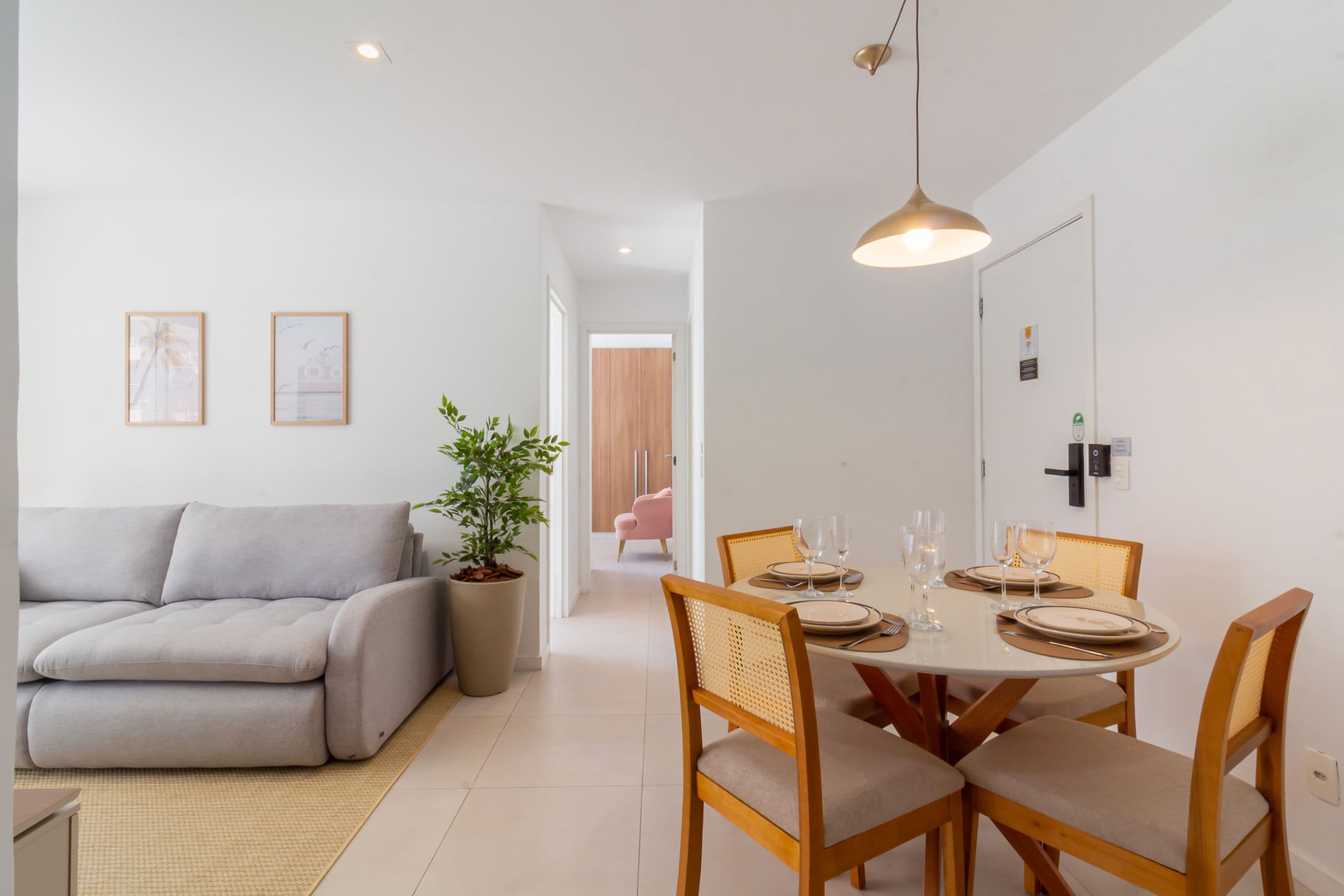 Una sala moderna con un sofá gris, una mesa de comedor para cuatro personas y una planta en maceta.