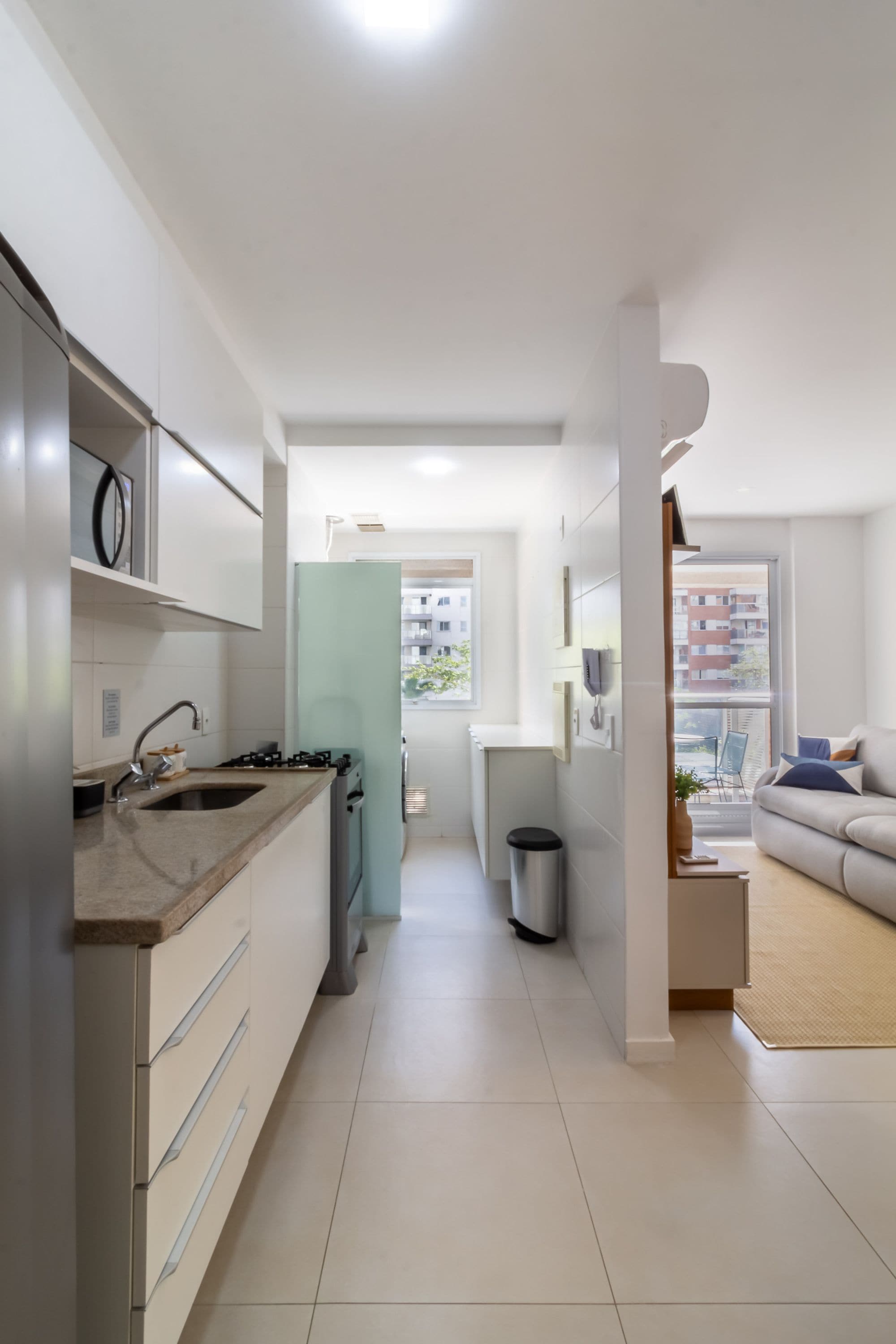 Una cocina moderna con horno empotrado y lavamanos, que da paso a una sala de estar con sofá y vistas al exterior.