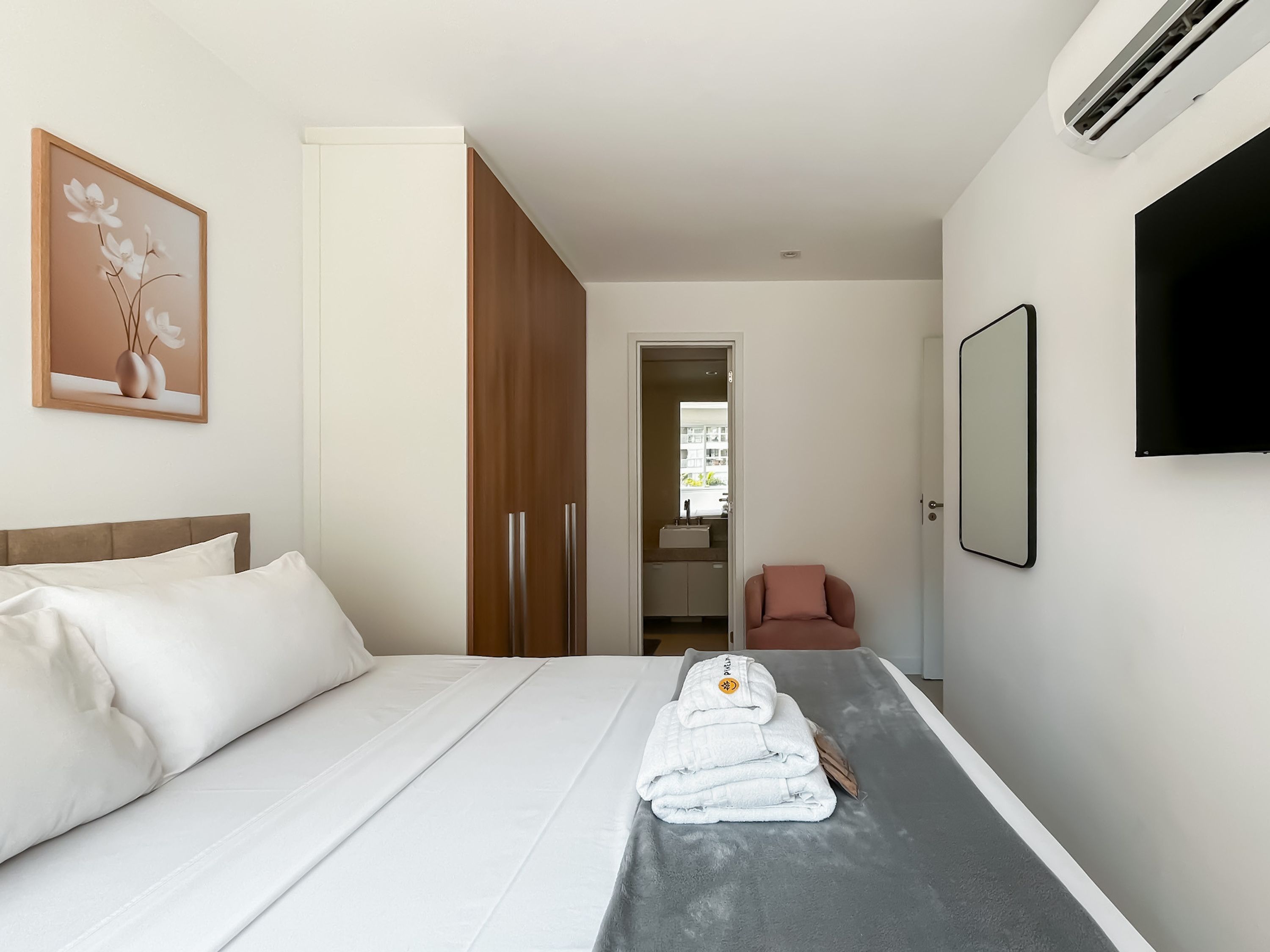 A hotel room with a bed, a chair, a TV, and a wardrobe.
