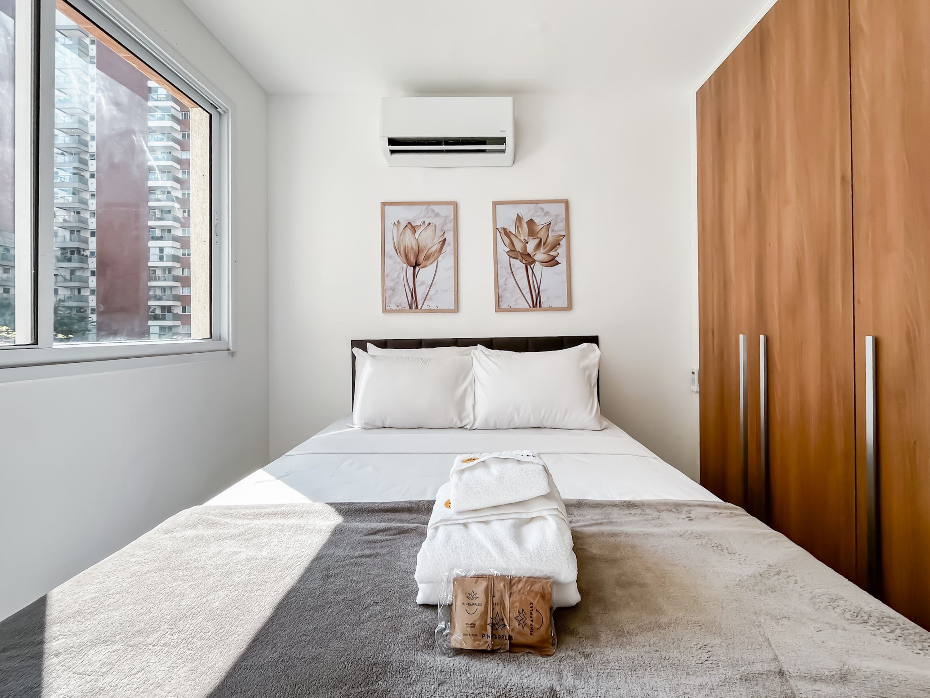 Un dormitorio moderno con una cama grande, ropa de cama blanca, un tapete gris y una ventana con vistas a edificios.