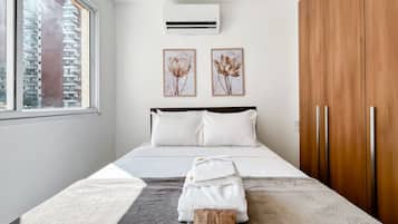 Un dormitorio moderno con una cama grande, ropa de cama blanca, un tapete gris y una ventana con vistas a edificios.
