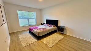 A bedroom with a bed, two bedside tables, a window with blinds, and a door. - Peaceful 3-bedroom house with AC in charming Palm Coast (Palm Coast)