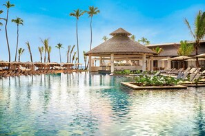 A resort pool with lounge chairs, palm trees, and a thatched-roof pavilion. - Romantic get away to Secrets Tides Punta Cana in the Dominican Republic (Playas)