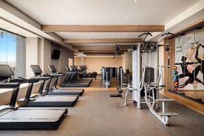 Un gimnasio con cintas de correr, máquinas de pesas y una pared decorada con un mural de temática fitness.