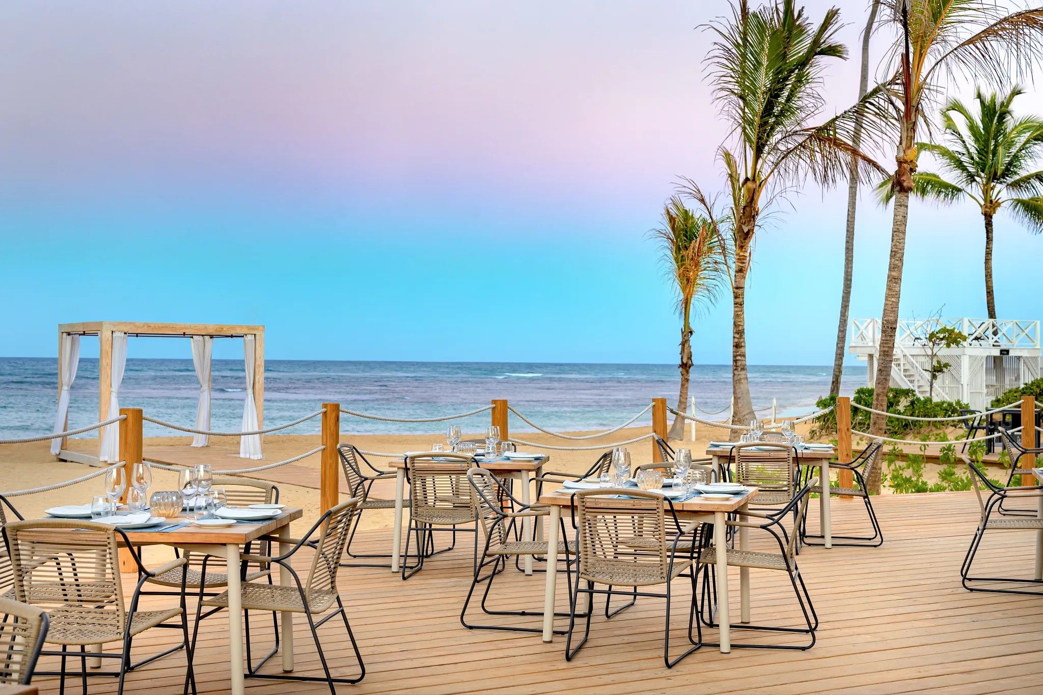 A beachside dining area with tables and chairs, overlooking the ocean.