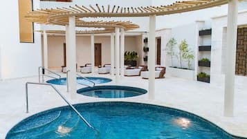 En indendørs swimmingpool med flere niveauer af siddepladser og en pergola i bambus.