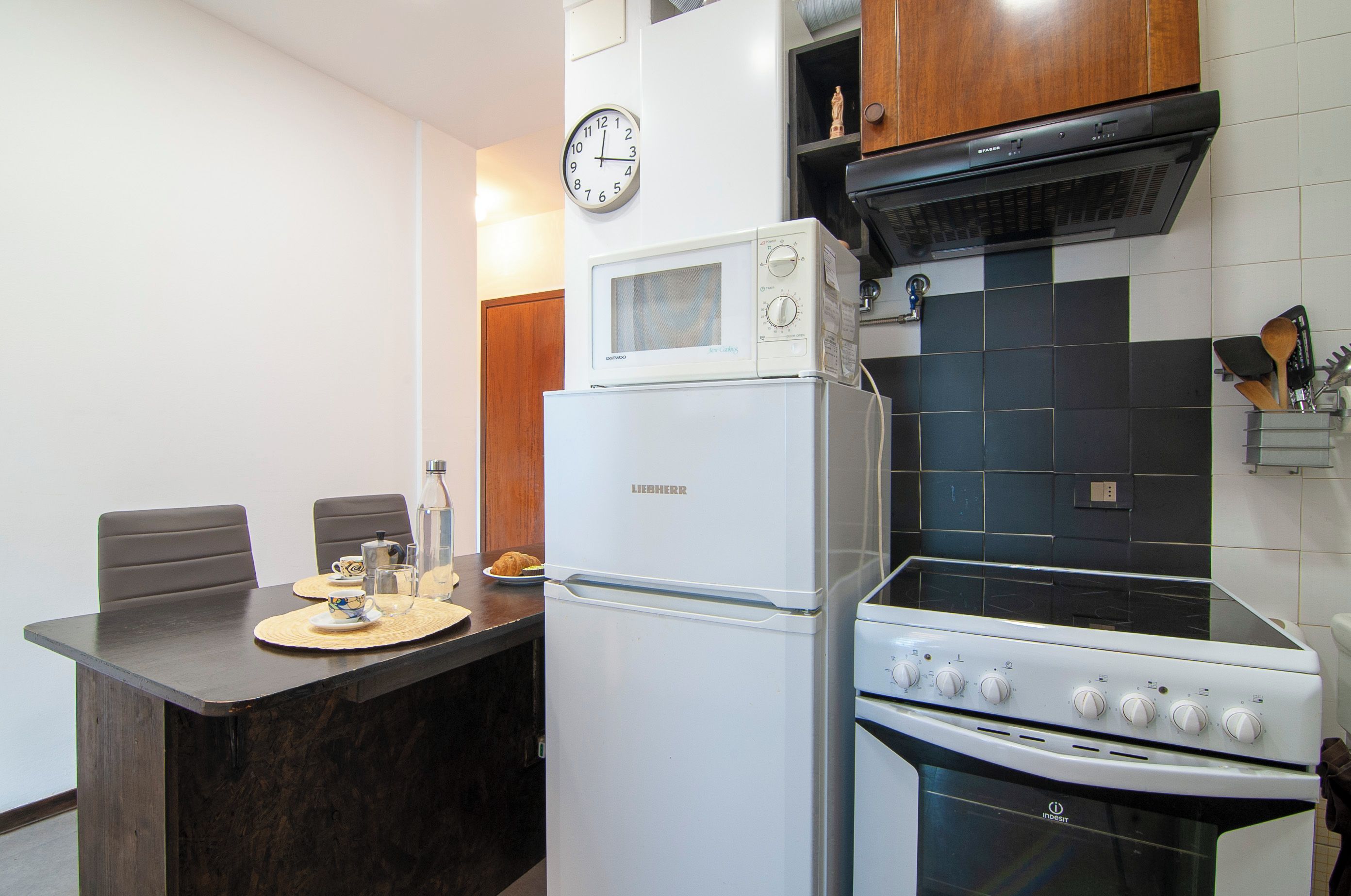 Cocina compacta con refrigerador, microondas, estufa y un reloj en la pared.
