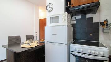 Cocina compacta con refrigerador, microondas, estufa y un reloj en la pared.