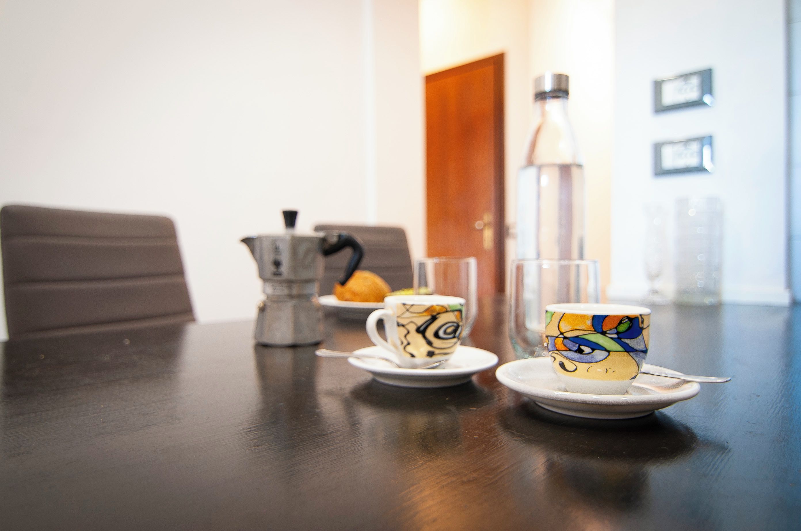 A dining table with two cups and a teapot, a bottle of water, and a door in the background.