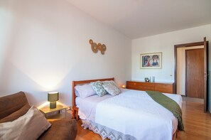 Una camera da letto con un letto, un comodino, una lampada, una cassettiera in legno, una porta e un addobbo a parete.
