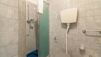 Ein Badezimmer mit Dusche, Toilette und einem blauen Mülleimer.