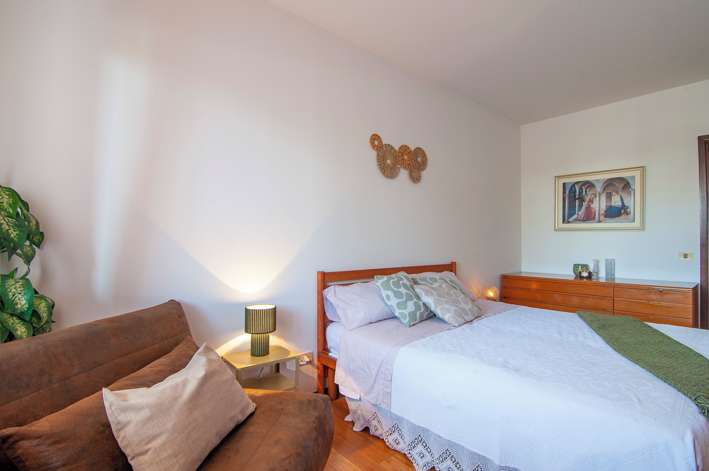 A bedroom with a bed, a nightstand, a lamp, a wooden dresser, and a framed picture on the wall.