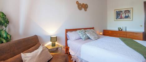 A bedroom with a bed, a nightstand, a lamp, a wooden dresser, and a framed picture on the wall.