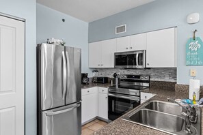 A modern kitchen with stainless steel appliances, white cabinets, and a granite countertop. - Beachfront 2BR+Bunks | Gulf View & Lagoon Pool (Panama City Beach)