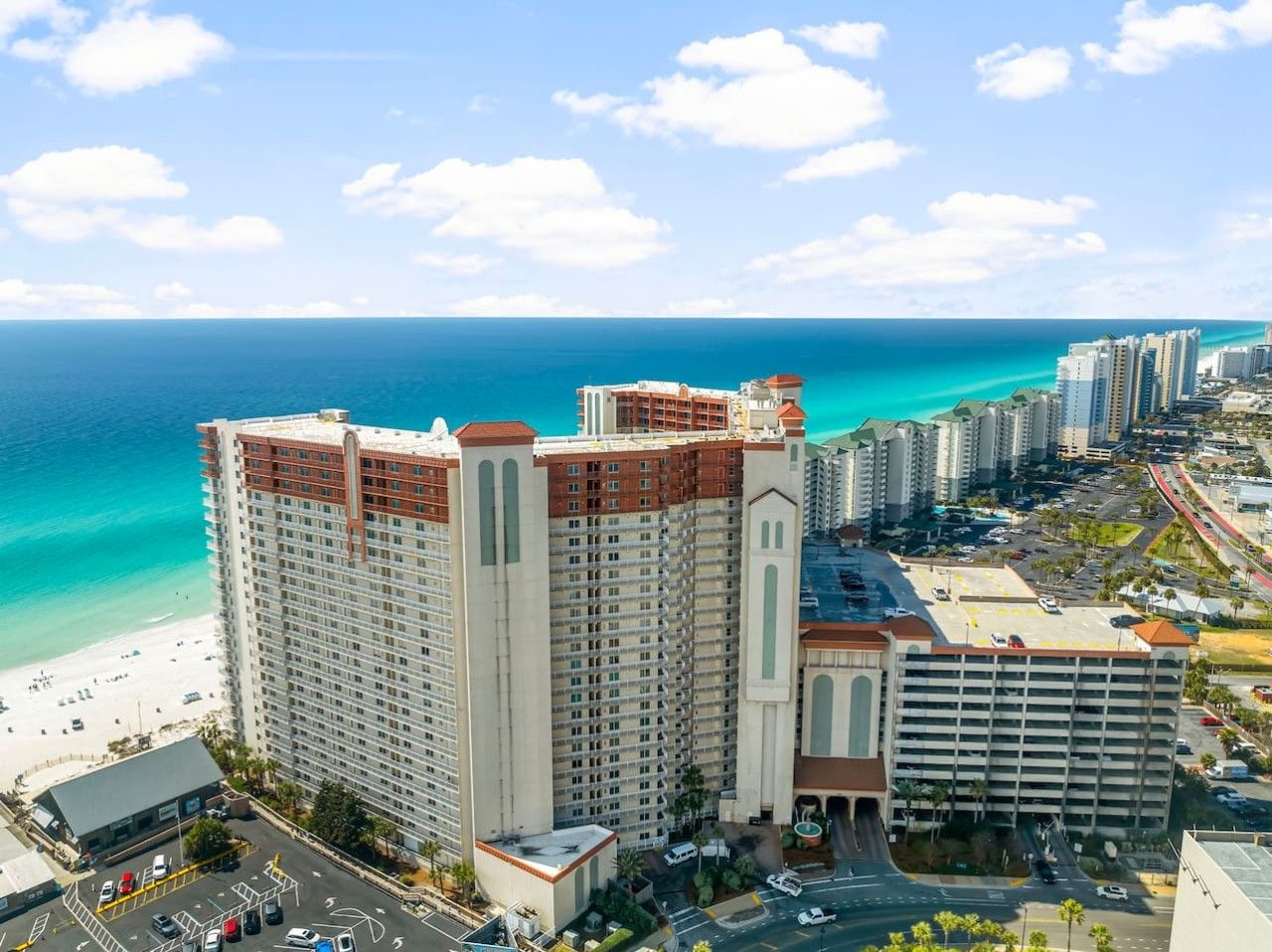 A high-rise hotel with multiple floors, a parking area, and a view of the beach and ocean.