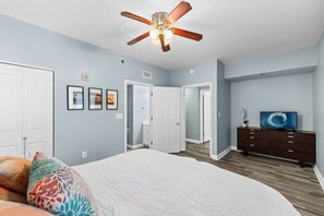 Une chambre à coucher avec un lit, une commode, un ventilateur de plafond et un téléviseur.
