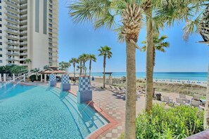 A hotel pool area with a clear view of the beach and ocean, surrounded by palm trees and lounge chairs. - Beachfront 2BR+Bunks | Gulf View & Lagoon Pool (Panama City Beach)