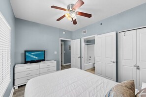 Une chambre à coucher comprenant un lit, un téléviseur, un ventilateur de plafond et un dressing.