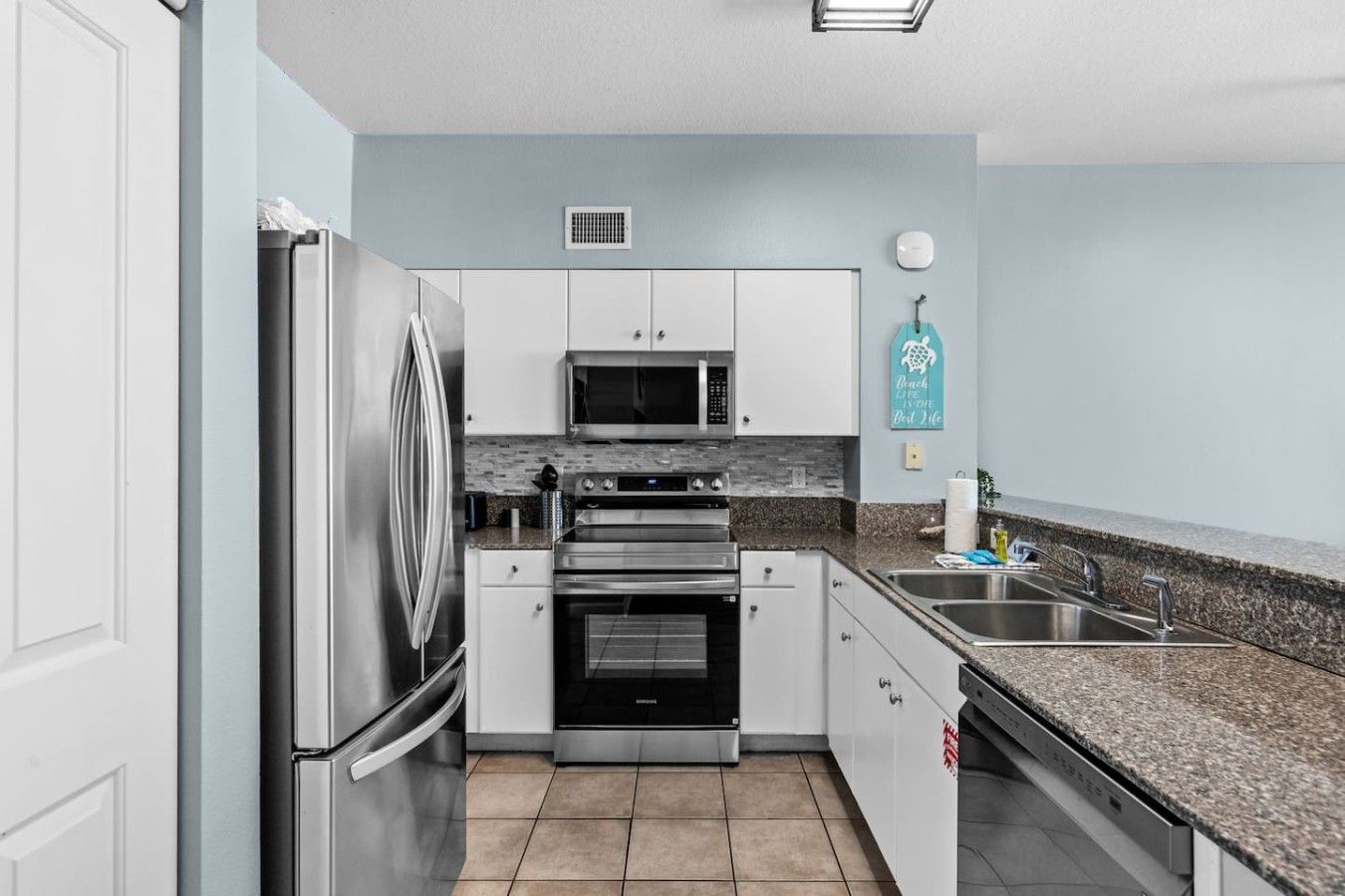 A modern kitchen with stainless steel appliances, a granite countertop, and light blue walls.