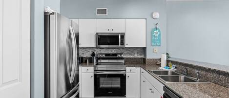 A modern kitchen with stainless steel appliances, a granite countertop, and light blue walls.