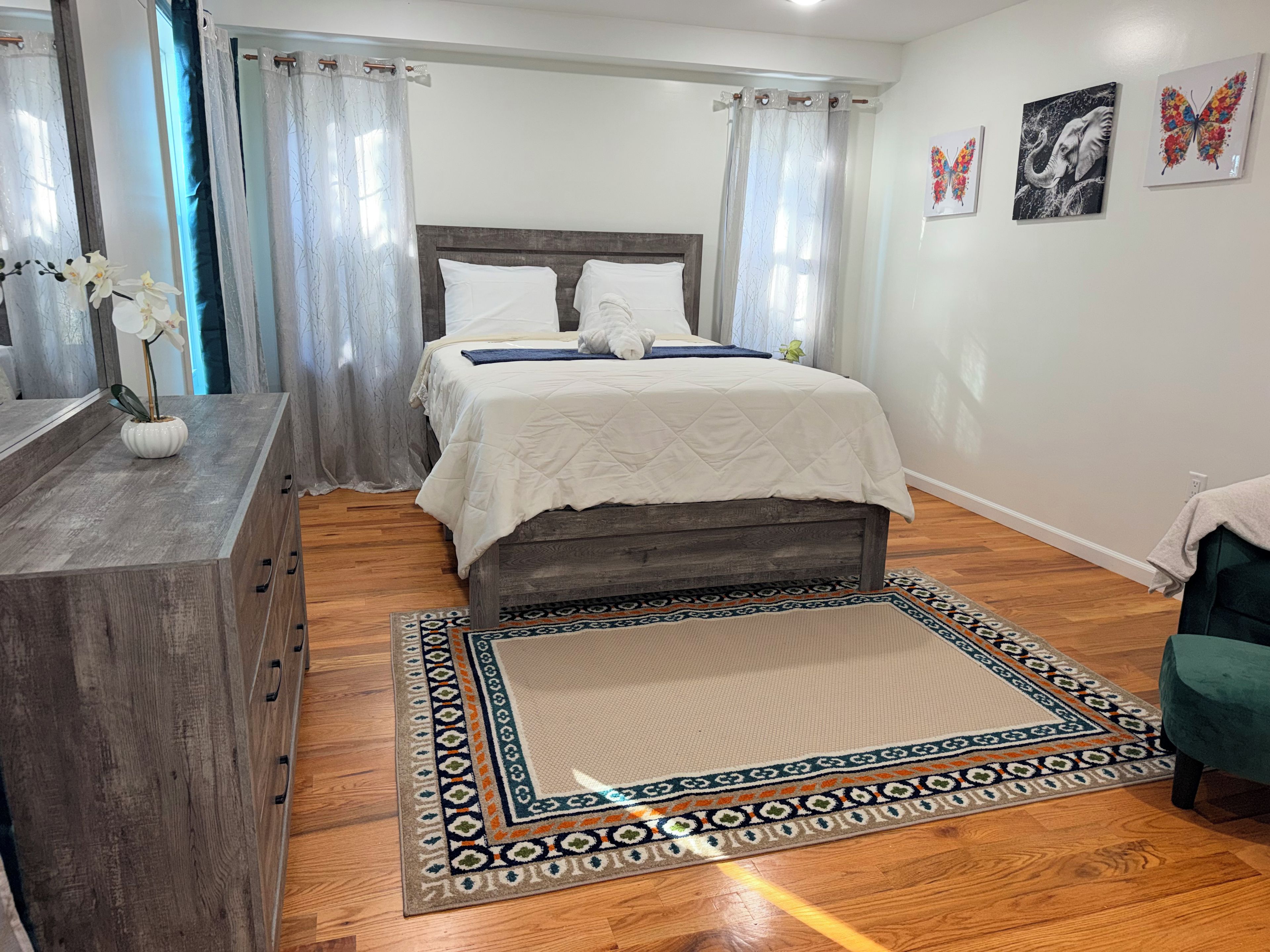 Un dormitorio con cama, cómoda, alfombra y obras de arte en la pared.