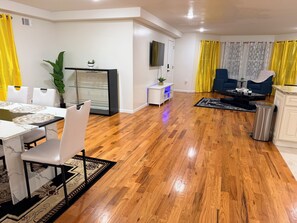 A modern living room with a dining area, wooden flooring, and yellow curtains.