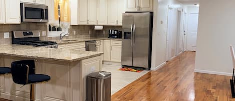 A modern kitchen with white cabinetry, stainless steel appliances, and a wooden floor.