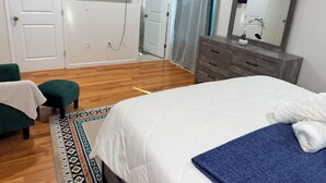 Une chambre à coucher comprenant un lit, une commode, un téléviseur fixé au mur et une porte donnant sur une autre pièce.