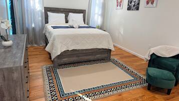 A bedroom with a bed, a nightstand, a chair, a rug, and artwork on the wall.