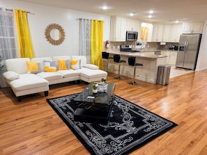 Una sala de estar moderna con un sofá, una mesa de centro y una zona de cocina con refrigerador, microondas y taburetes de bar.