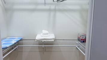 A walk-in closet with a metal shelving unit, a blue patterned shelf, and a white towel stack.