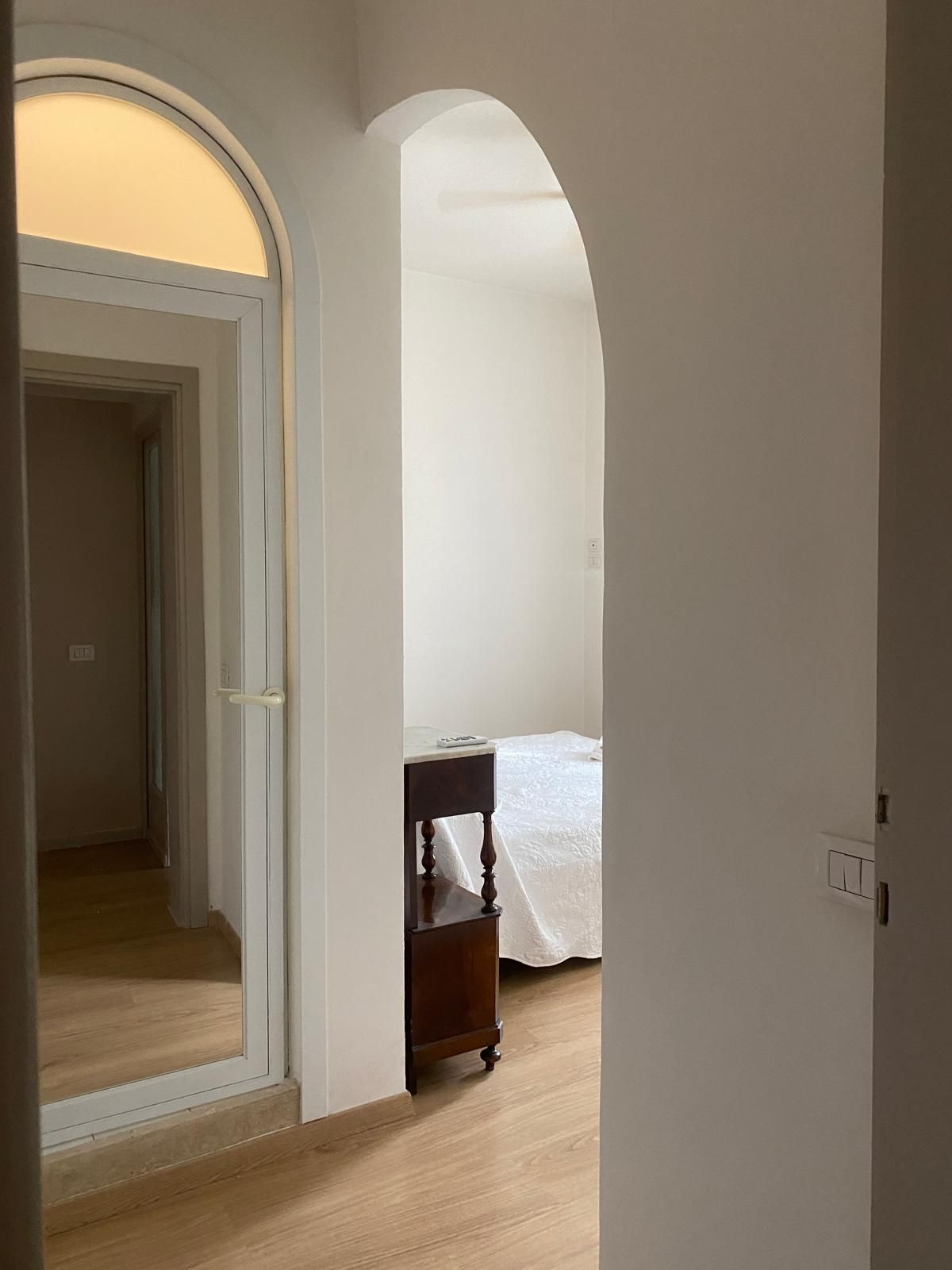 A hallway leading to a bedroom with a bed and a nightstand.
