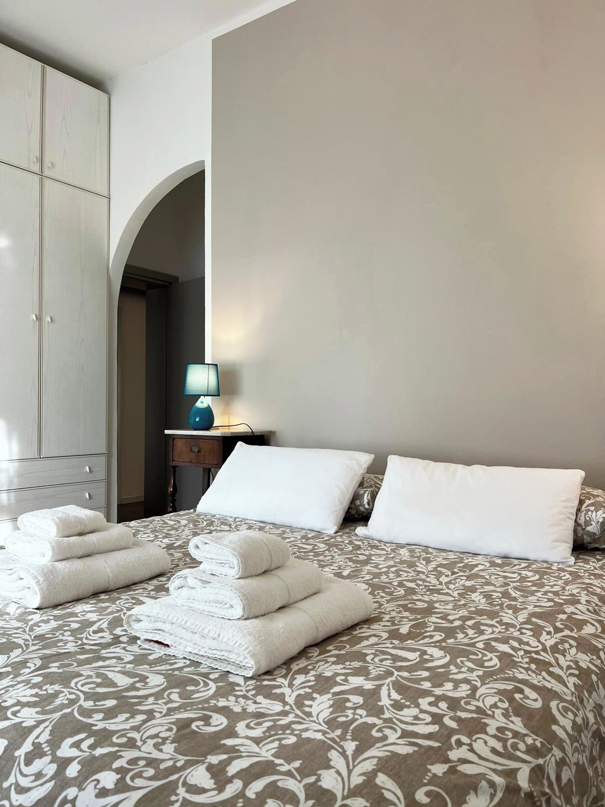 A hotel room with a bed, a wardrobe, and a nightstand with a lamp.