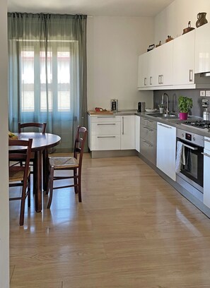 A modern kitchen with white cabinets, a dining table with chairs, a window with sheer curtains, and a view of a body of water. - Spacious, bright apartment with parking in the Da Pia neighborhood (Spello)