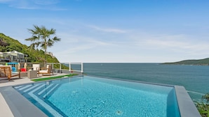Ein Pool mit Blick auf das Meer, umgeben von Stühlen und einem kleinen Garten.