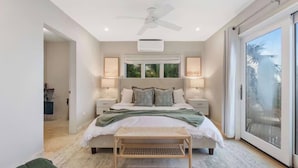 Ein Schlafzimmer mit einem großen Bett, zwei Nachttischen, einem Deckenventilator und einer Glastür zum Balkon.