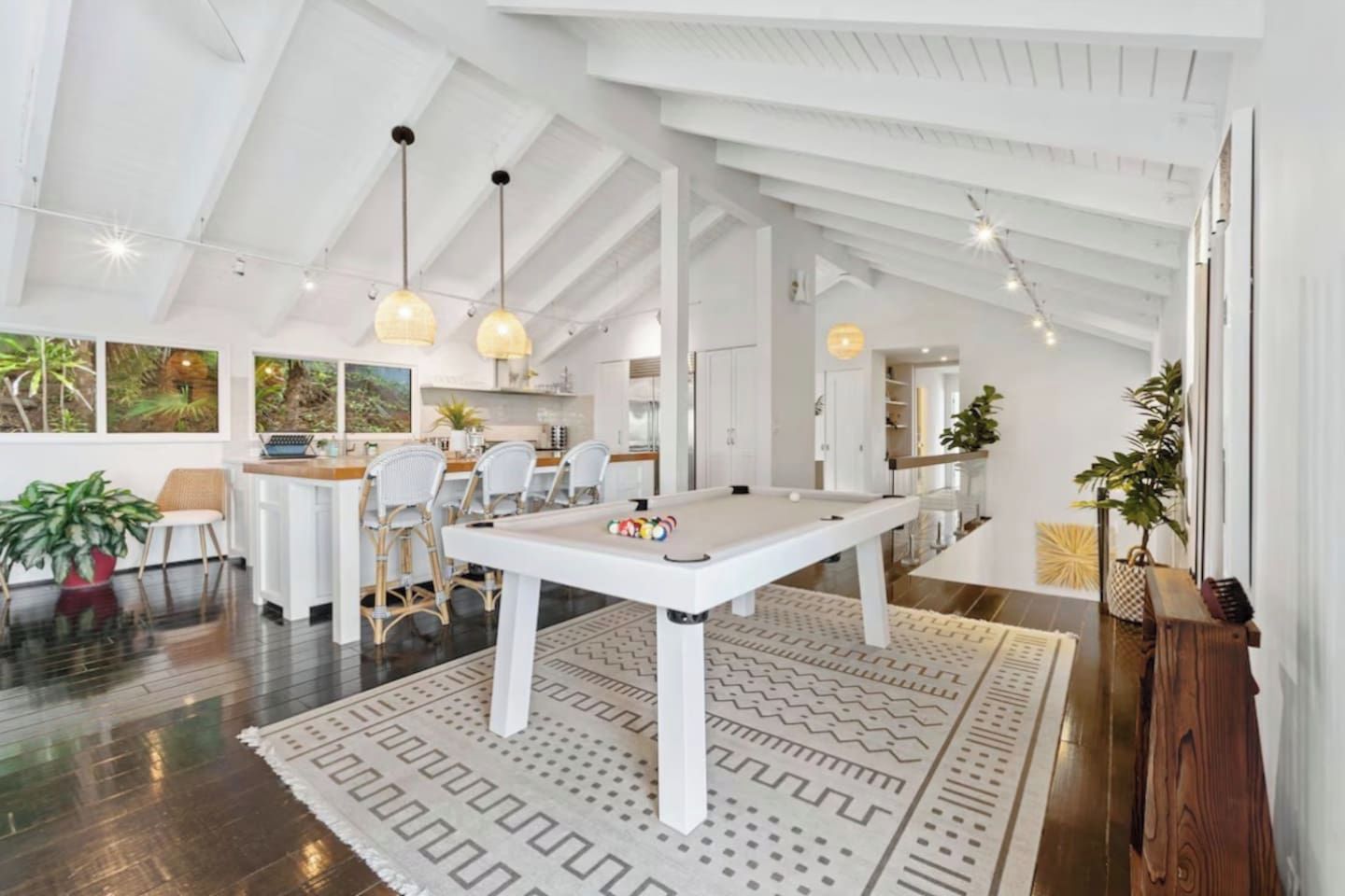 A spacious room with a pool table, white furniture, and pendant lighting.