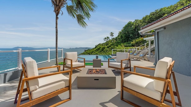 Eine Terrasse mit Sitzgelegenheiten im Freien, einer Feuerstelle und Blick auf das Meer und die Hügel.