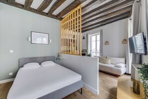A modern bedroom with a bed, a sofa, a TV, and a wooden ceiling. - Bright Studio 2P - Louvre / Palais Royal (Paris)