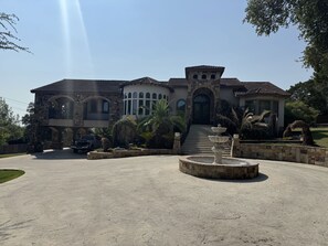 Una casa grande de varios pisos con fachada de piedra, una fuente central y un camino de entrada.