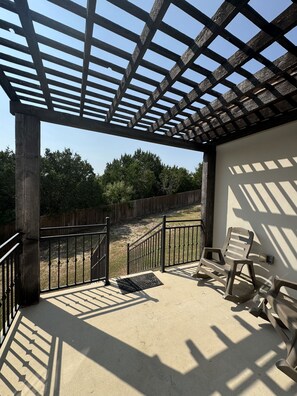 Un espacio de patio cubierto con un pérgola, una valla de madera y una silla.