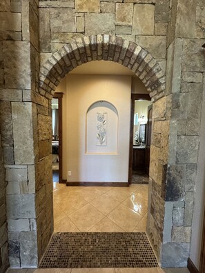 Un arco de piedra que da acceso a una habitación con suelo de baldosas y un adorno en la pared.
