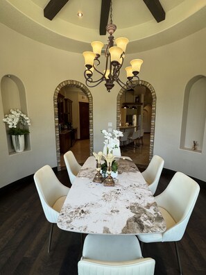 Un comedor con una mesa de mármol, sillas blancas, una araña y un arco.