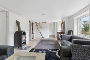 A modern living room with a fireplace, a staircase, and a view through a large window. - Lovely holiday home near Asnæs, Zealand (Asnæs)