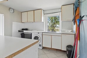 Une cuisine de taille réduite, équipée d’un lave-linge, d’un évier et de placards.