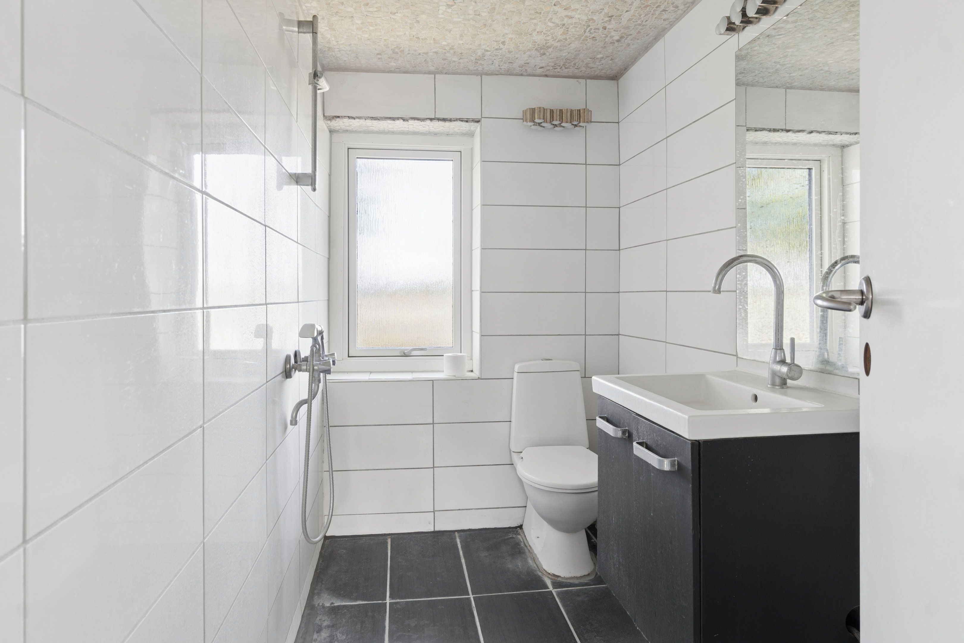 Une salle de bain avec des murs carrelés de carreaux blancs, un sol carrelé de carreaux noirs, des toilettes, un lavabo et une douche.
