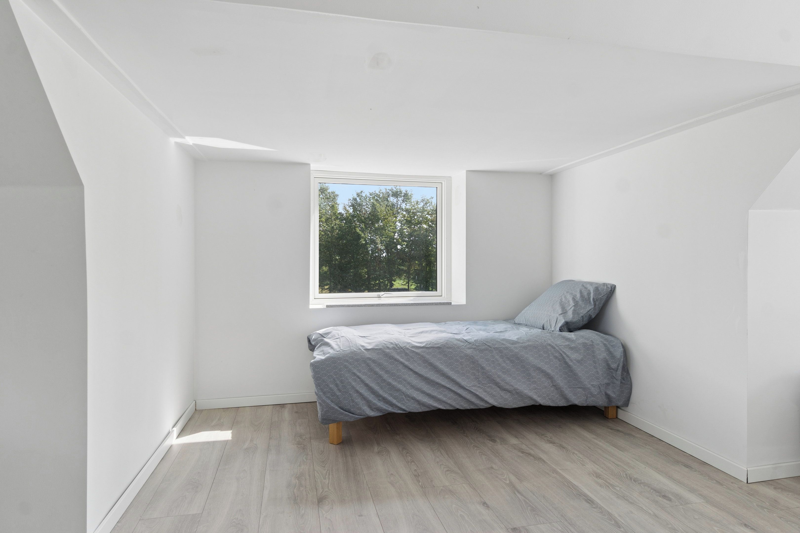 A small, unoccupied attic bedroom with a single bed, a window, and sloped ceiling.