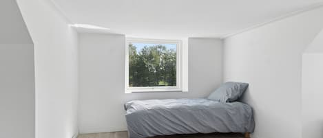 A small, unoccupied attic bedroom with a single bed, a window, and sloped ceiling.